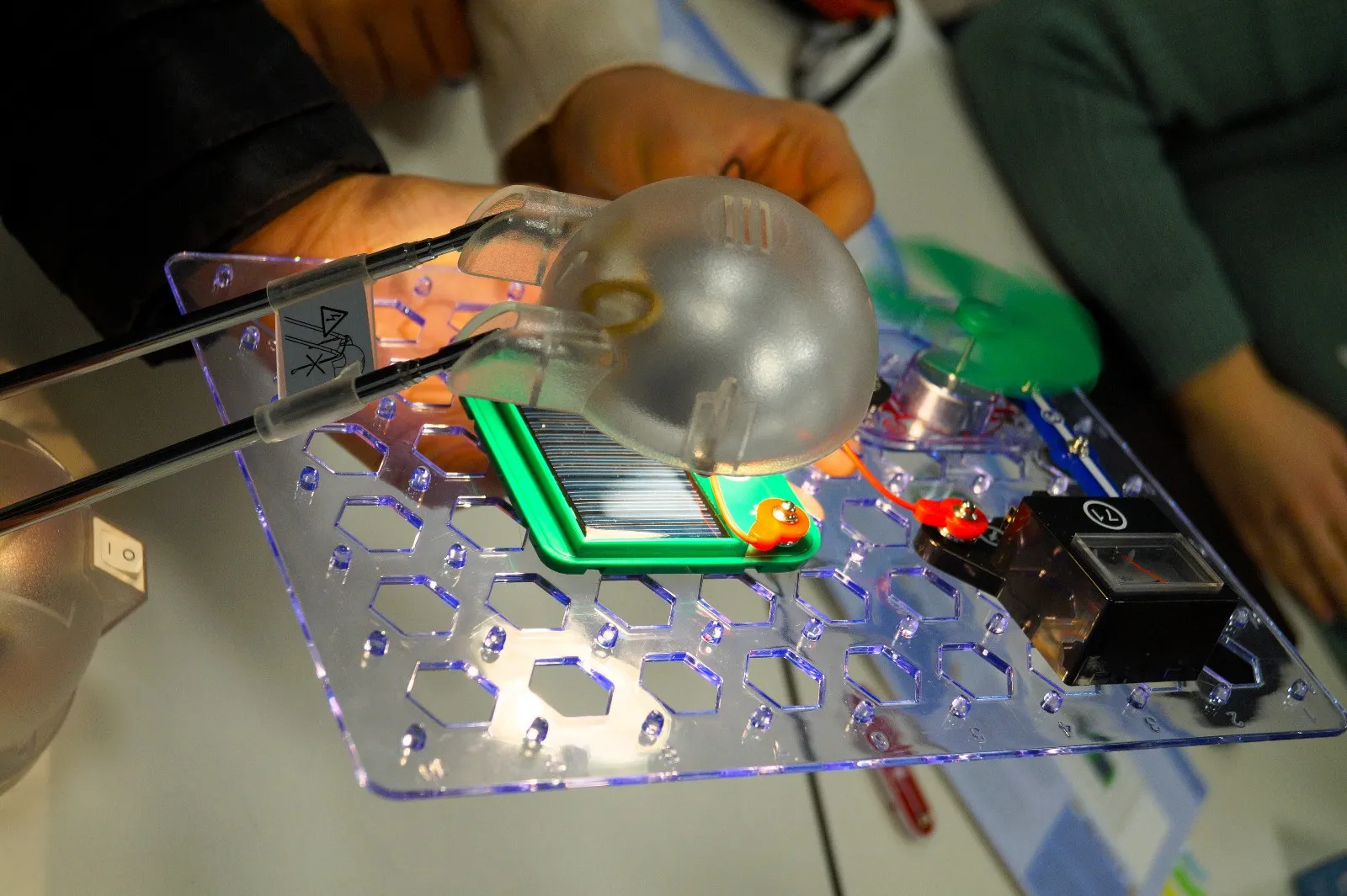 Hände halten bei einem Versuch eine Lampe über eine Solarzelle auf einer Experimentierplatte mit Strommessgerät