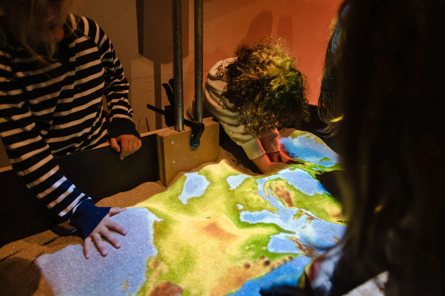 Kinder spielen an der Sand-Box, ein Höhenrelief wird farbig projiziert