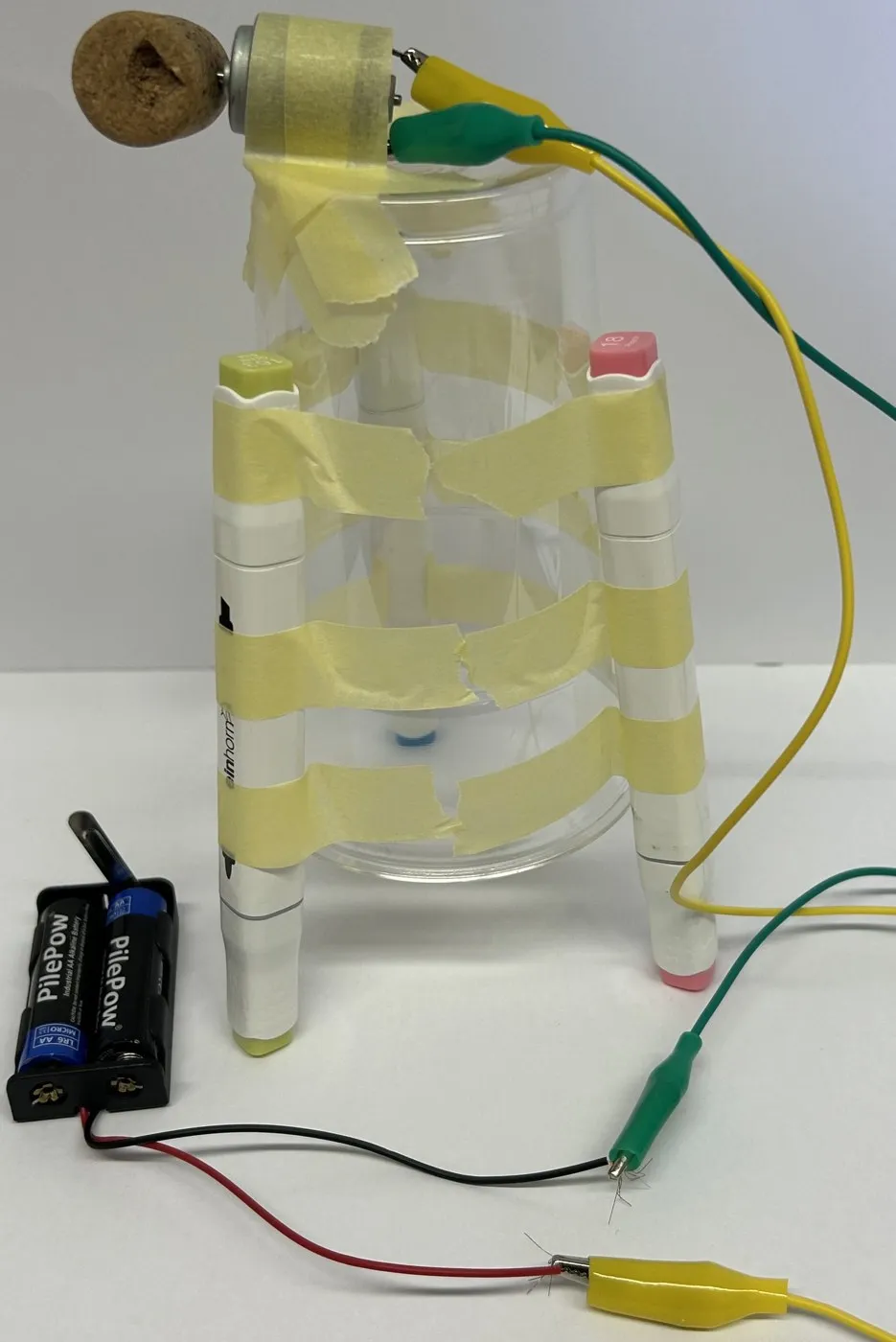 Selbstgebauter Kritzelroboter: Ein Becher mit drei Filzstiften als Beinen, oben ein Motor mit Korken, verbunden mit Krokodilklemmen und Batteriegehäuse