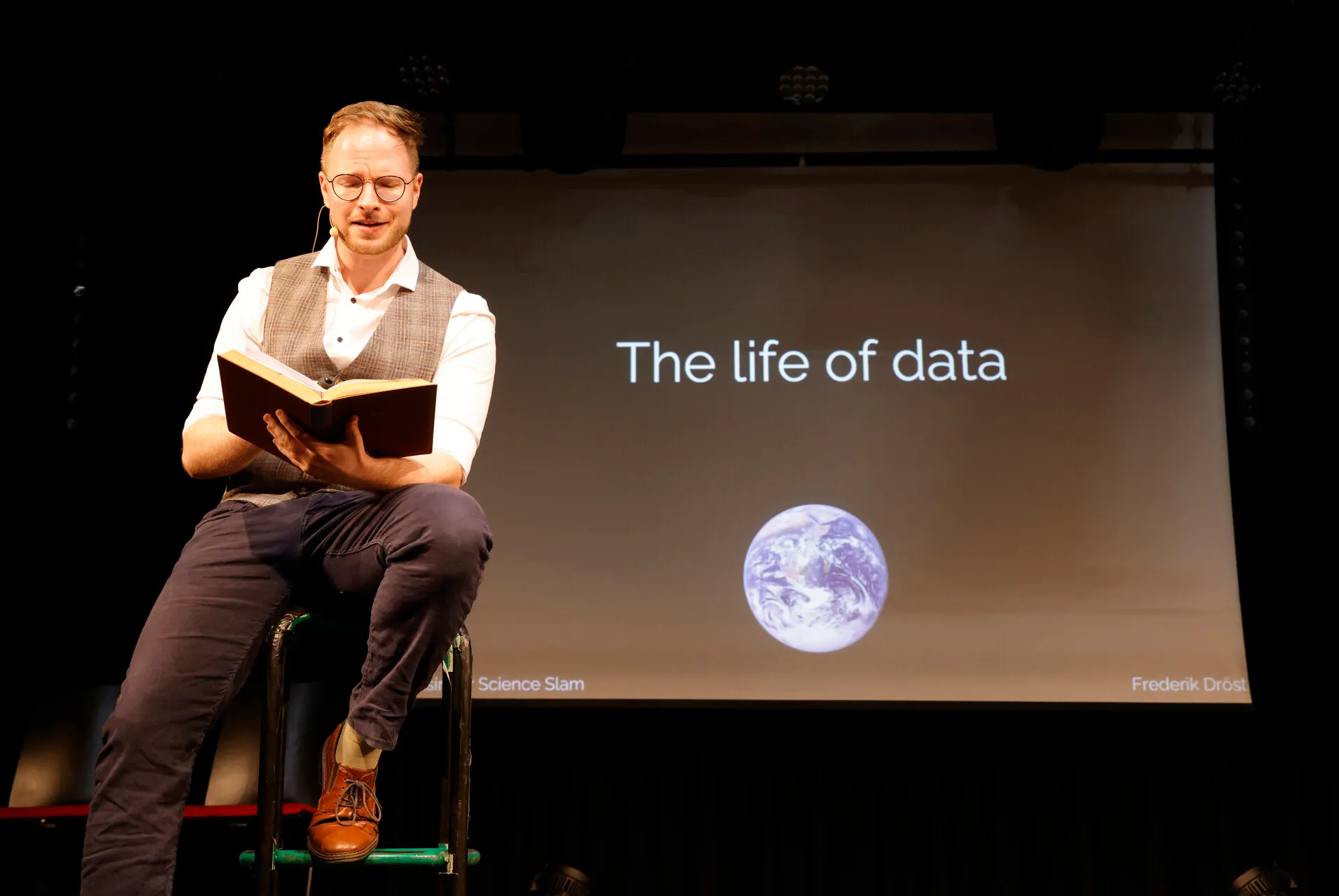 Slam Warm-up außer Konkurrenz: Frederik Dröst liest aus einem dicken Buch vor, im Hintergrund die Folie „The life of data“