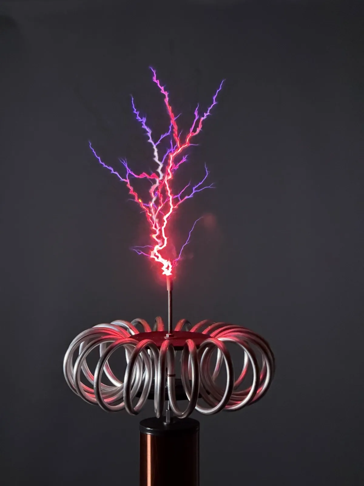 Tesla-Spule mit leuchtenden violetten und roten Blitzen vor dunklem Hintergrund
